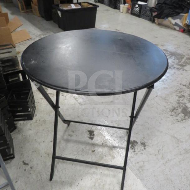 Black metal foldable table, round top, 24x28.5 inches. Used condition, sturdy frame, compact storage design.