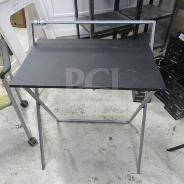 Foldable metal and pressboard table, 25x18x31 inches, black top, lightweight frame, good condition, ideal for compact spaces.