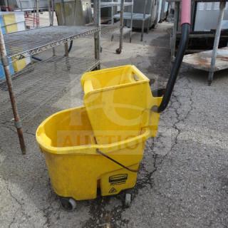 Yellow mop bucket with wringer, black handle, on wheels; shows wear. Suitable for commercial cleaning duties.