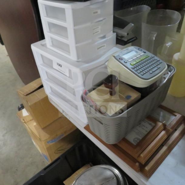 A lot of various office supplies including a label maker, plastic drawers, wooden stamp, and framed documents.
