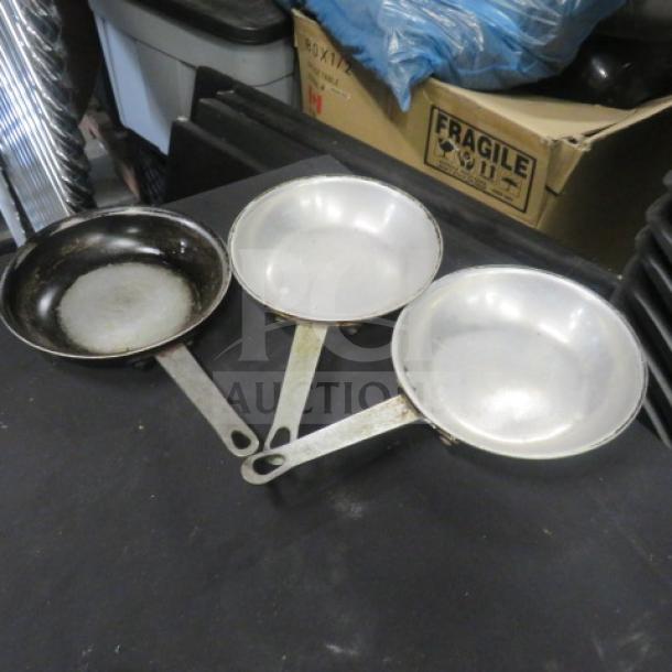 Three 7.5-inch sauté pans with metal handles; two in fair condition and one heavily used. No visible brand markings.