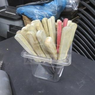 A lot of assorted steak knives with wooden handles, stored upright in a clear container. Some handles are red. Condition appears used.