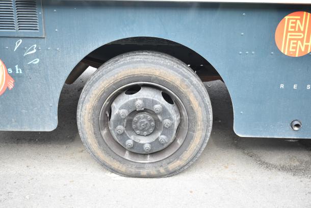 2002 Freightliner MT45 food truck wheel close-up; blue Ludicrous wrap with visible logo graphics; in used condition.