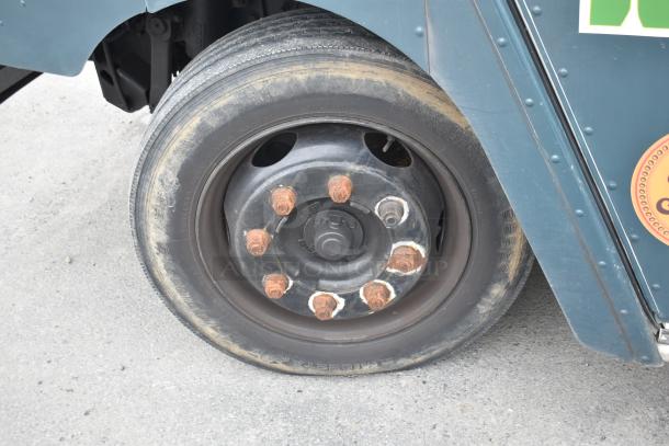 Close-up of a 2002 Freightliner MT45 food truck wheel, showing a black rim with rusted lug nuts.