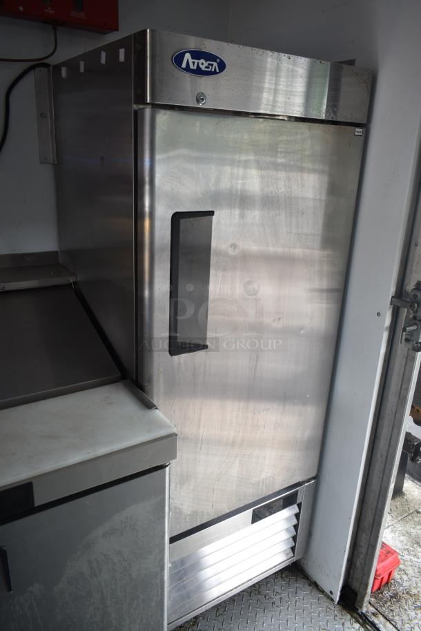 Stainless steel Atosa refrigerator inside a food truck with a visible black handle and Atosa logo on top.