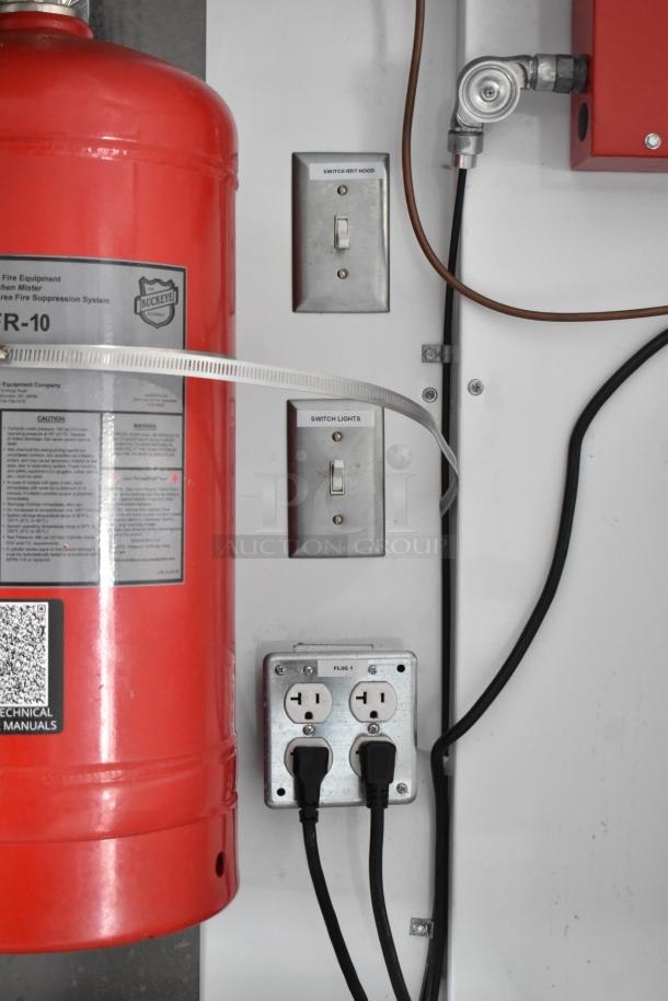 Red fire suppression system tank labeled "Buckeye KR-10," metal switches labeled "Switch Vent Hood" and "Switch Lights," and dual outlets with cords plugged in.