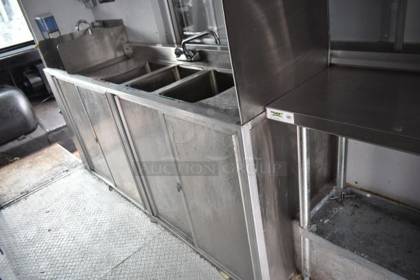 2002 Freightliner MT45 food truck interior with stainless steel sink, prep area, storage, and clean flooring.