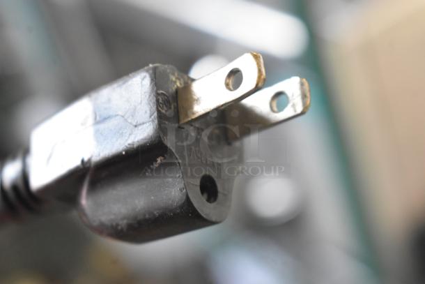 Close-up of a metal prong from a Cadco Unox XAF003 convection oven's power plug, showing 120V label.