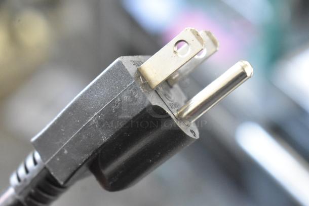 Close-up of a standard black power plug belonging to a Cadco Unox XAF003 convection oven, showing metal prongs.