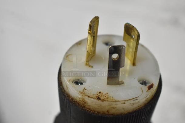 Close-up of a power plug with visible wear, featuring three metal prongs and a white plastic base.