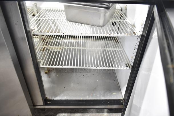 True TSSU-72-30M-B-ST prep table interior view with shelves and a stainless steel container. Cabinets show signs of wear.