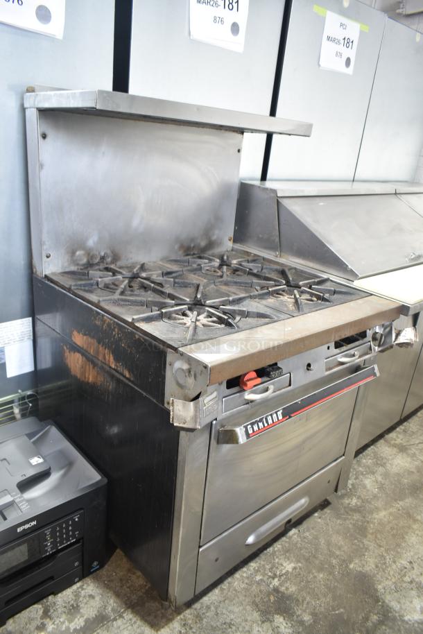 Garland commercial gas 4-burner range with oven, over shelf, and backsplash in used condition. Visible wear on surface.