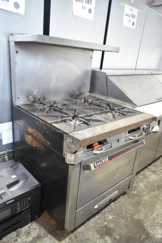 Garland commercial gas 4-burner range with oven, over shelf, and backsplash in used condition. Visible wear on surface.