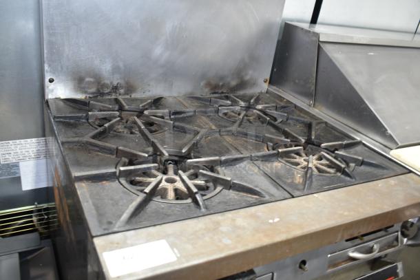 Garland commercial gas-powered 4-burner range with oven, over-shelf, and backsplash; used condition, visible wear.