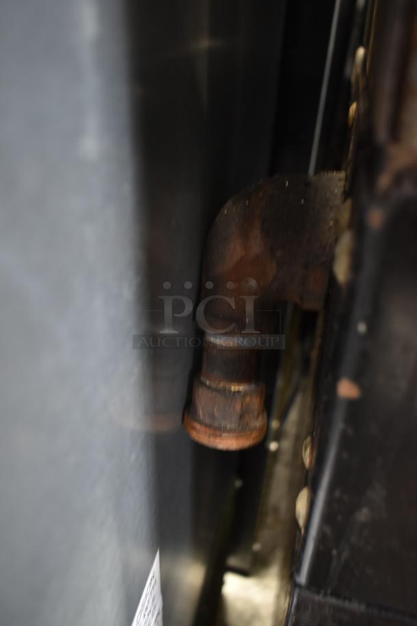 Garland commercial gas 4-burner range with oven, overshelf, and backsplash. Features visible gas connection. Condition not specified.