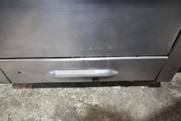 Garland commercial gas range, 4 burners with oven, over shelf, and backsplash, stainless steel, signs of use visible.