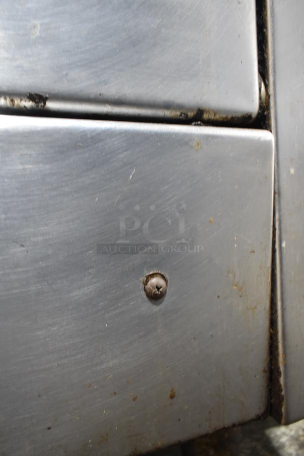 Close-up of Garland commercial gas range with visible wear and screw. Stainless steel surface with some dirt and residue.