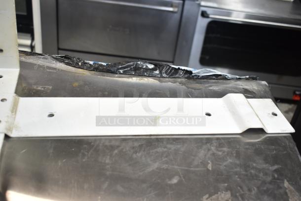 Metal piece in used condition, possibly a bracket, with four holes for mounting, on a stainless steel surface.