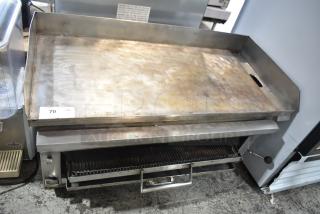 Commercial gas-powered flat top griddle with cheese melter, stainless steel, fair condition, warning label visible.