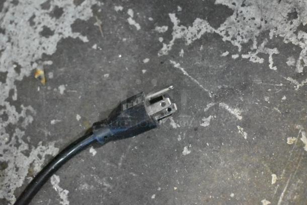 A black three-prong power plug on a rough gray surface, associated with a Manitowoc SD0452A Ice Machine.