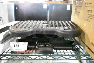Textured black footrest on shelf with auction label "114." Features non-slip surface and adjustable mechanism.
