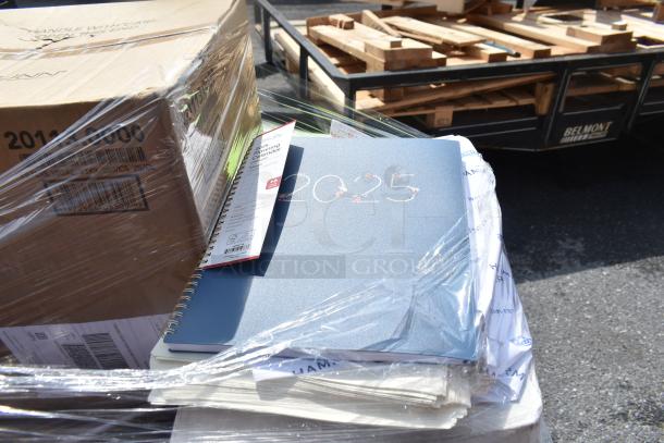 Plastic-wrapped pallet with blue 2025 planner, labeled calendar, and cardboard boxes. New scratch and dent auction items.