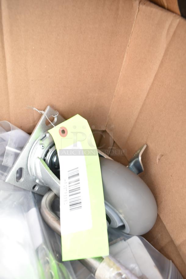 Cardboard box containing assorted scratch and dent items including a caster wheel with metal mount, green tag, and various components.