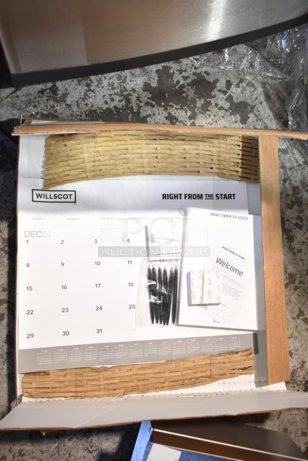 Eight new Willscot calendars in cardboard box, includes pens and welcome inserts. Some packaging damage visible.