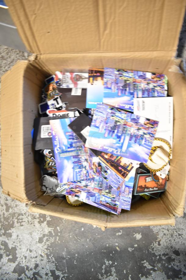 Lot of Texas-themed items including postcards, pins, spoon, shot glasses in a cardboard box; various conditions.