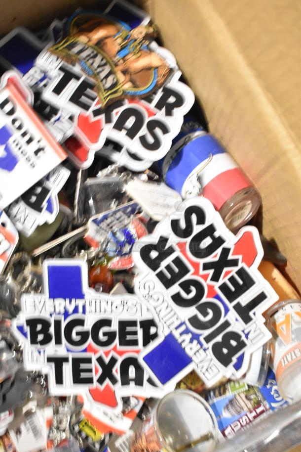 Box of various Texas-themed items including paraphernalia, pins, shot glasses, and a spoon. Visible stickers read "Everything's Bigger in Texas."