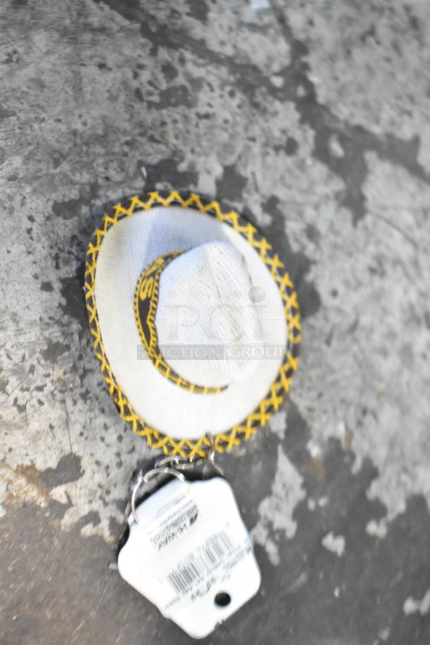 Close-up of a small woven sombrero with yellow embroidery and attached tag, part of a Texas-themed auction lot.