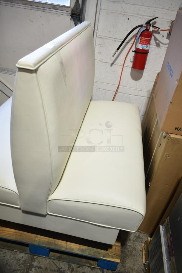 White double-sided booth seat, leather upholstery, in good condition, placed on a pallet in a storage area.