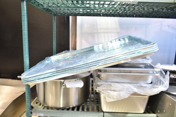 14 Brand New Scratch and Dent items on a shelf, including various sizes of premium, anti-jam stainless steel hotel pans and aluminum bun pans.