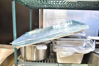 14 Brand New Scratch and Dent items on a shelf, including various sizes of premium, anti-jam stainless steel hotel pans and aluminum bun pans.