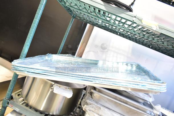 Stack of brand new perforated aluminum bun pans on a shelf; includes stainless steel steam table pans, various brands and sizes.