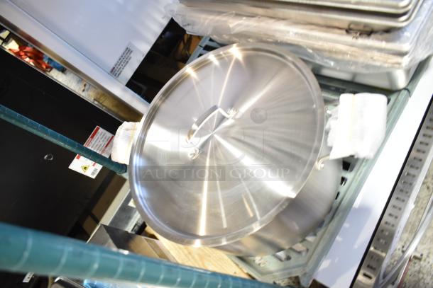 Stacked new kitchenware including stainless steel steam table pans and a large lidded pot. Factory wrap visible.