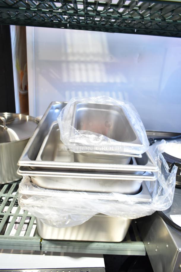 Stacked new stainless steel steam table pans, various sizes, wrapped in plastic, on a metal shelf.