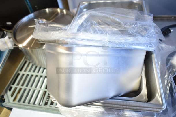 Assorted new kitchenware including stainless steel and aluminum pans, wrapped in plastic, featuring brands like Vollrath.