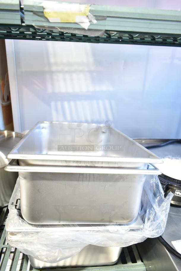 Stack of brand new stainless steel steam table pans, various sizes, visible 18" x 26" perforated aluminum sheet pan.