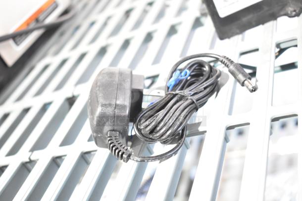 Black power adapter with coiled cable, model 020237-45, on a metal grid surface. Marks of wear visible.