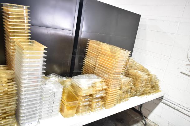 Lot of plastic containers, drop-in bins, and lids on a table. Various sizes, clear and amber hues. Appears in used condition.