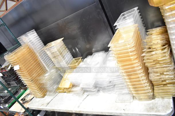 Lot of various clear and amber drop-in bins with lids, stacked on shelves. Ideal for storage.