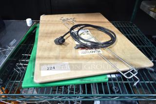 Three items including a large wooden cutting board, a green cutting board, and a black cable, on a metal shelf. Auction tag reads "224 JX3".