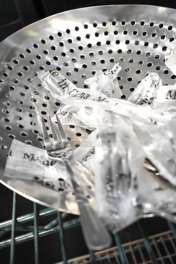Lot of various items including three tined forks, displayed in a stainless steel colander, wrapped in clear packaging.