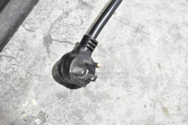 Black electrical plug of True GDM-72-HC cooler, shown on a textured gray surface.