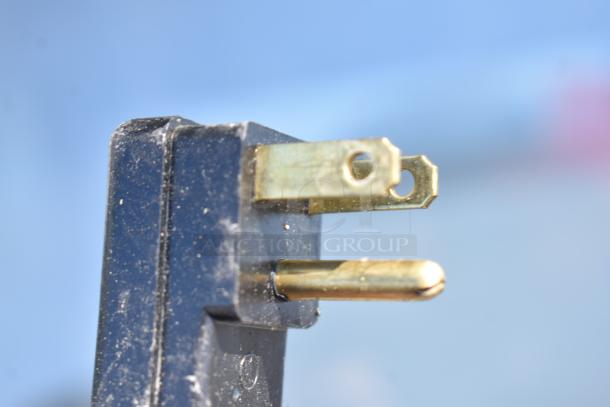 A close-up of a black electrical plug with brass prongs, part of a commercial ice cream dipping cabinet rated at 115 volts, 1 phase.