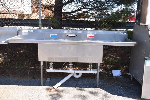 Duke Commercial 3 bay sink with dual drain boards, stainless steel, visible faucets, outdoor setting, good condition.