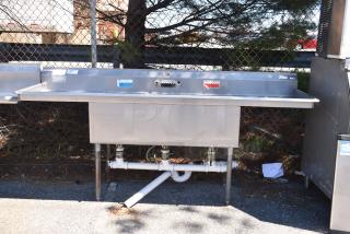 Duke Commercial 3 bay sink with dual drain boards, stainless steel, visible faucets, outdoor setting, good condition.