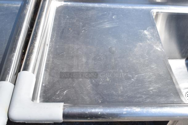 Commercial 3 bay stainless steel sink with dual drain boards, some surface scratches, sturdy construction.