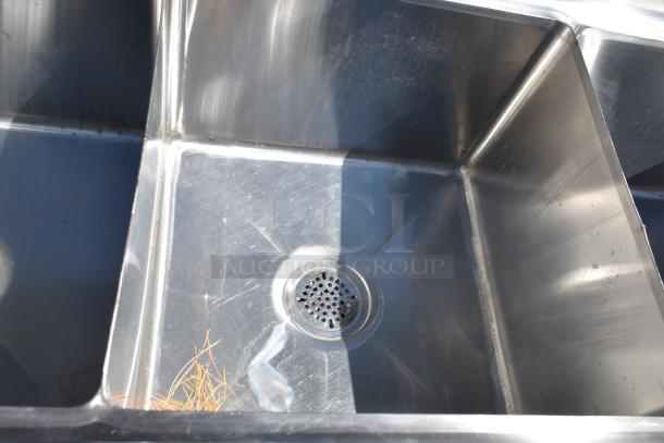 Commercial 3 bay stainless steel sink with dual drain boards, visible drain, used condition.
